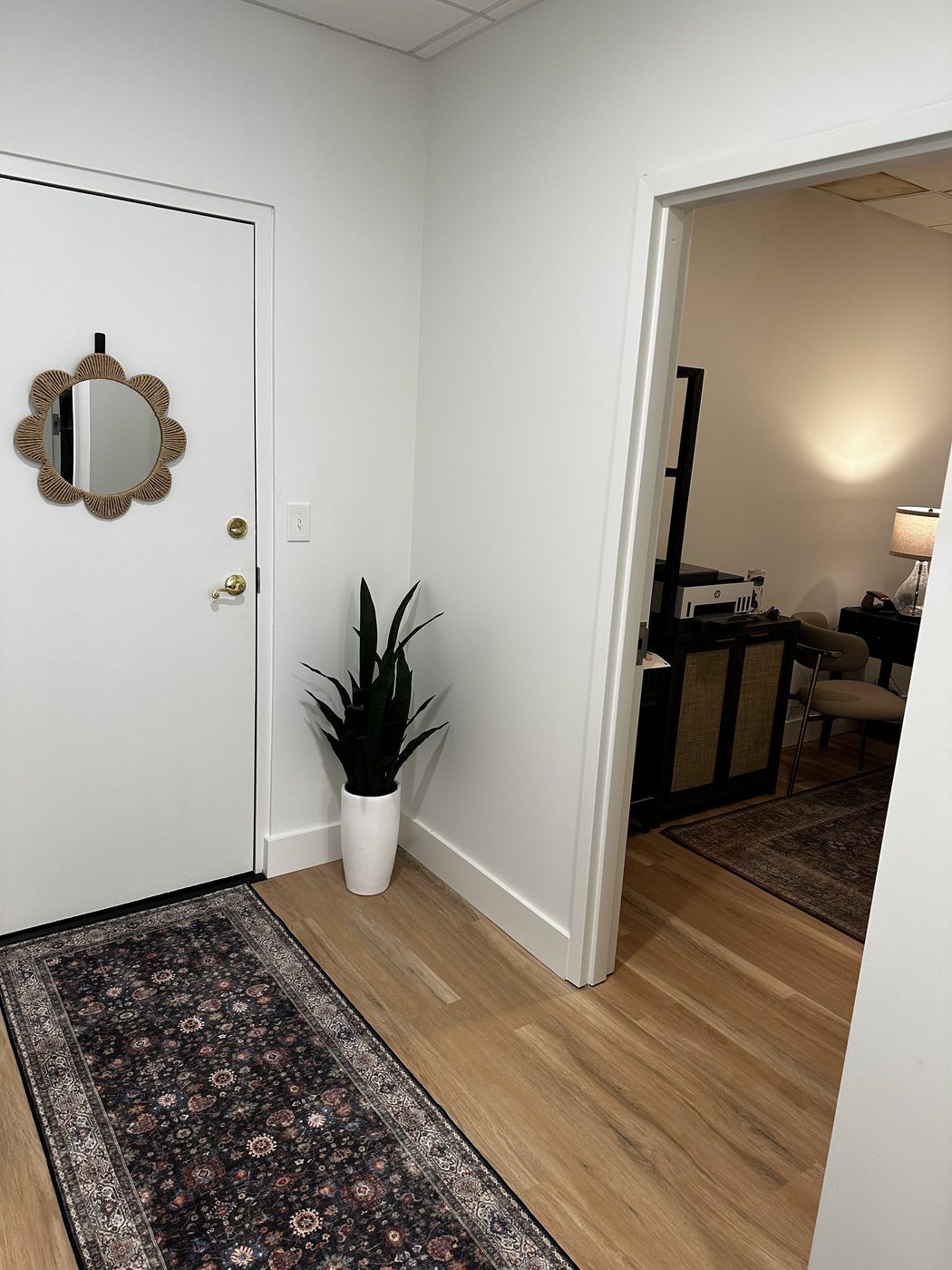 The door through to the bathrooms, with a scalloped mirror and a potted plant beside it, looking through to the office beyond